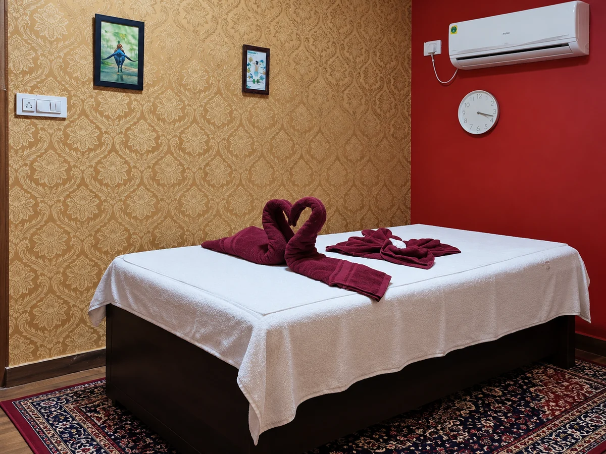 Single massage bed with white linens and burgundy towels beside gold damask wallpaper
